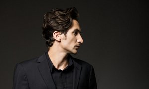 Man in a black suit with slicked-back short curly hair